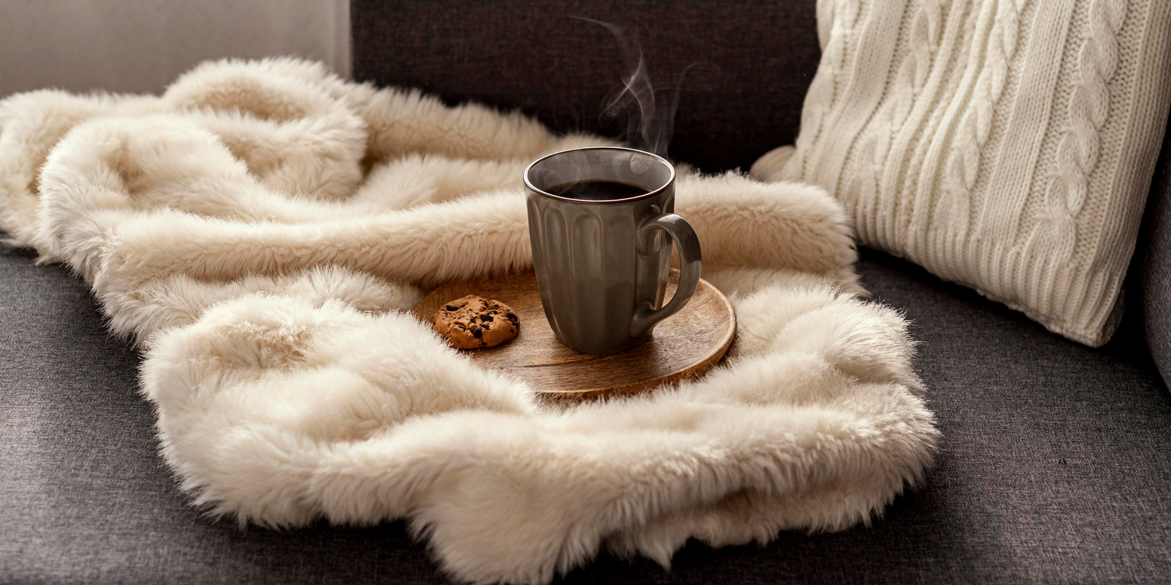 A cup of steaming coffee and a chocolate chip cookie on a wooden saucer, placed on a faux fur throw | Source: Freepik