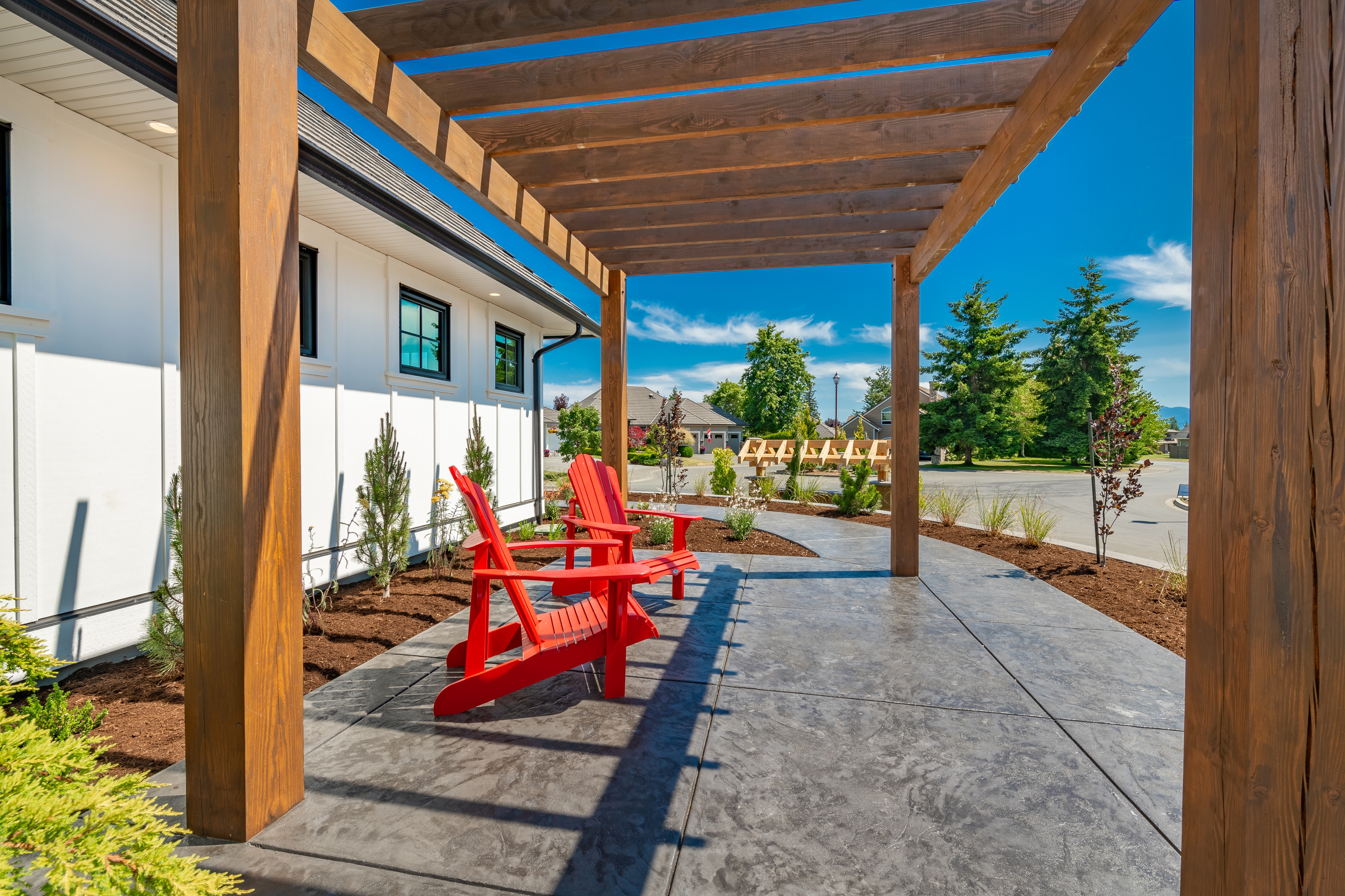 A patio with a pergola features stamped concrete and two wooden red chairs. | Source: Shutterstock