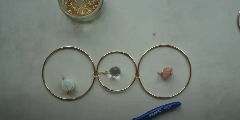 Once the chain and the middle crystal prism are connected to the same jump ring, attach the other end of the chain to the jump ring to the left of the middle hoop.  | Source: YouTube/Vanir Creations