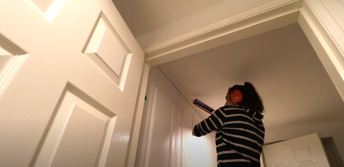 A woman applying caulk on wardrobe door joints | Source: YouTube/@TheCarpentersDaughterUK