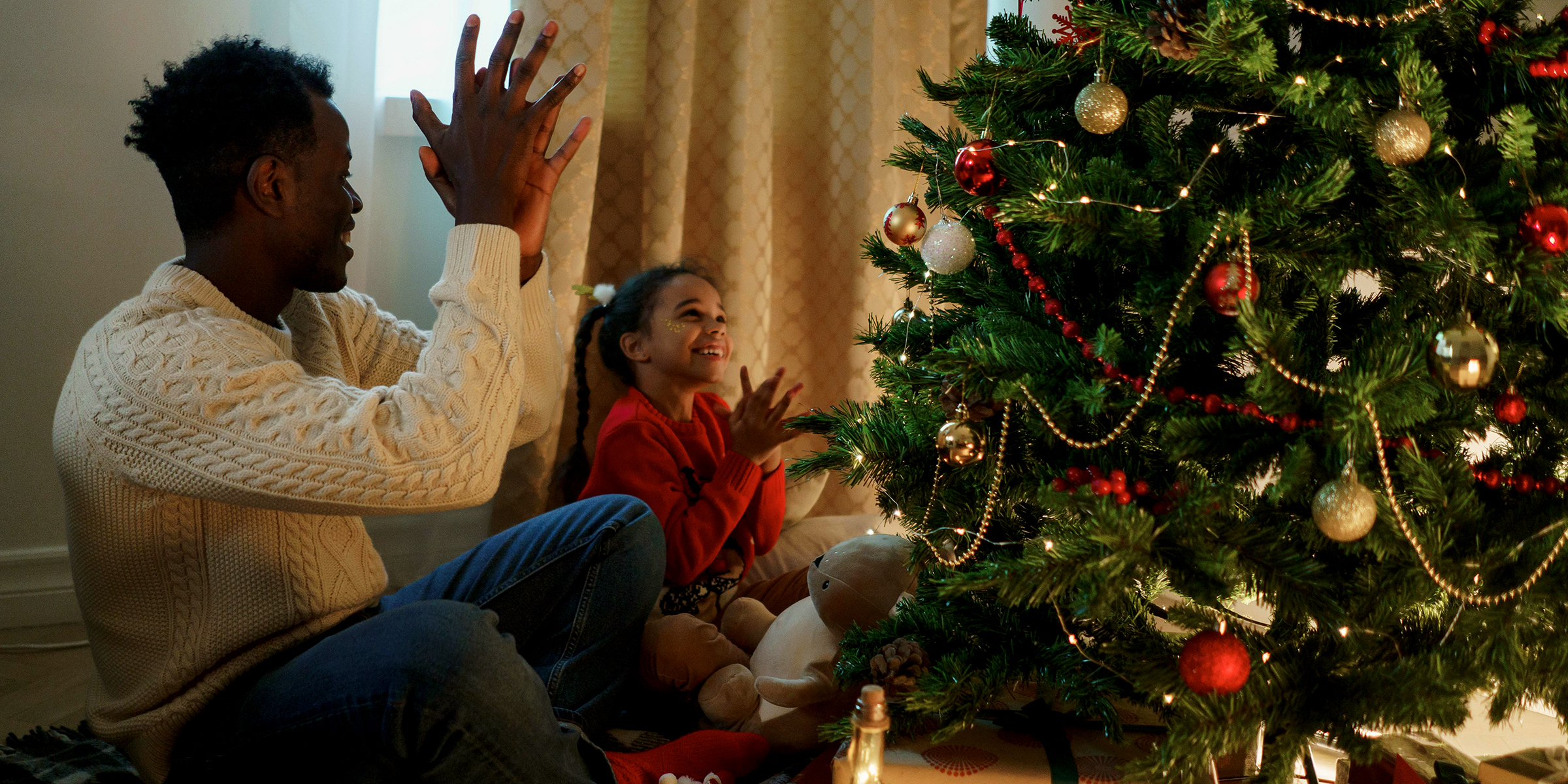 A father and daughter sitting by a Christmas tree | Source: Pexels